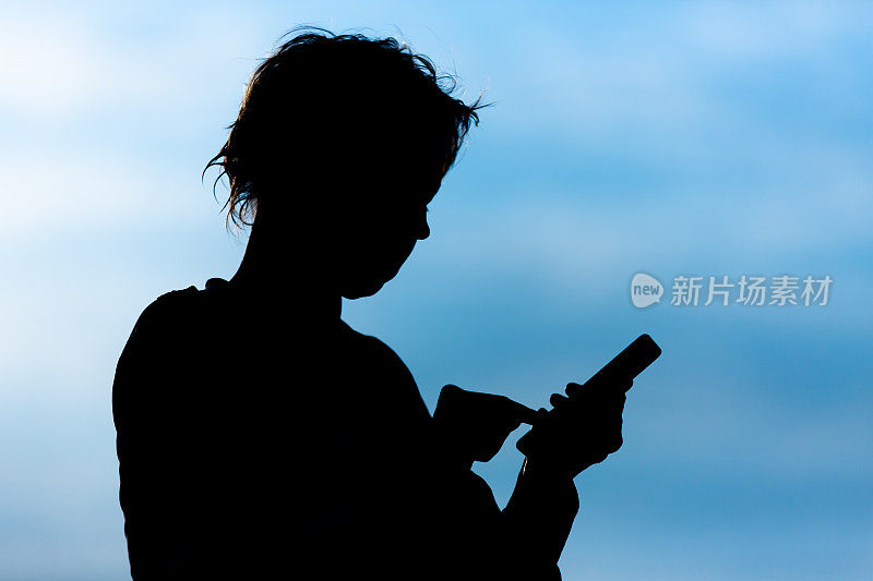 Silhouette of a woman typing on the phone screen, against the sky